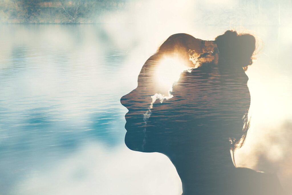 Ombre de la tête d'une femme devant un ciel bleu avec des nuages, ayant une photo en surexposition de lever de soleil dans la tête.